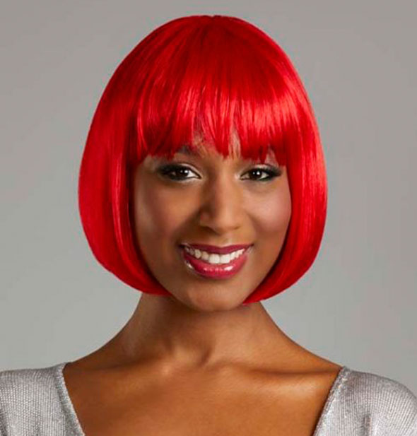 Model wearing a short, bright red wig with bangs.