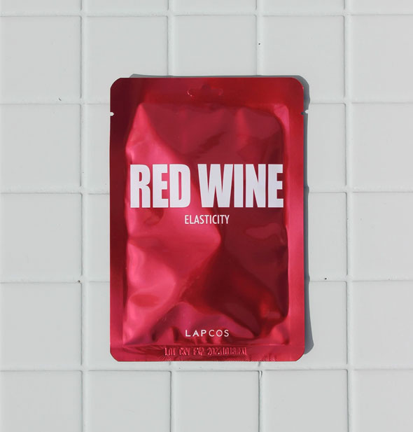 Red LAPCOS Red Wine Elasticity mask packet on white tile surface