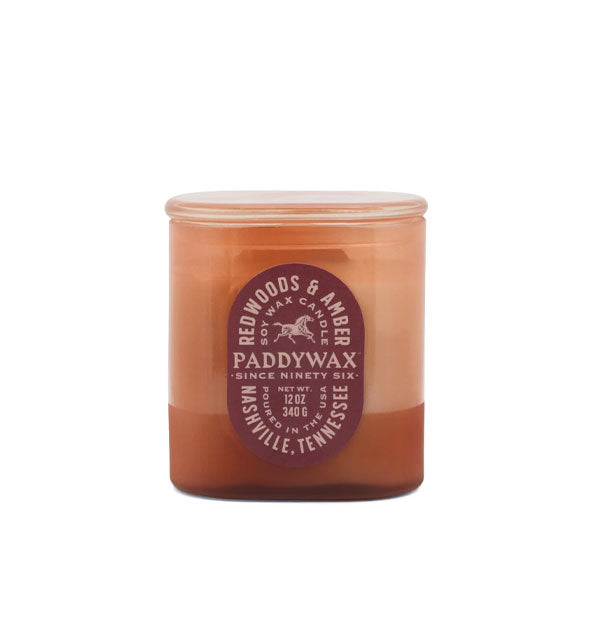 Amber-colored glass jar Redwoods & Amber Paddywax candle with oblong text-heavy maroon label