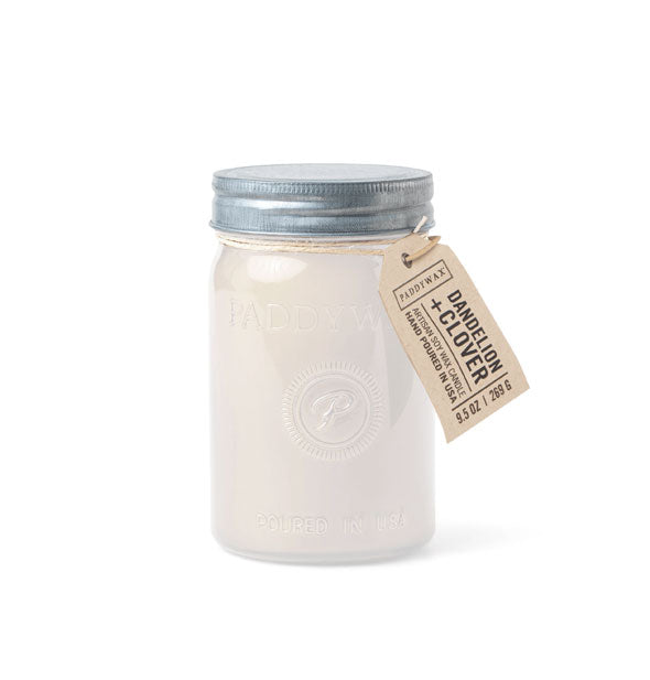 White wax candle in glass jar with metal lid and hanging tag that says, "Dandelion + Clover"