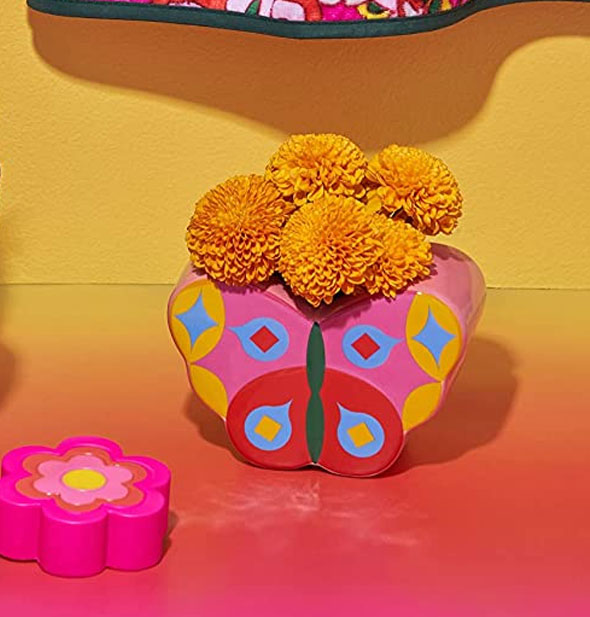 Butterfly vase holds a small bunch of orange marigolds against a yellow background with other retro-style items