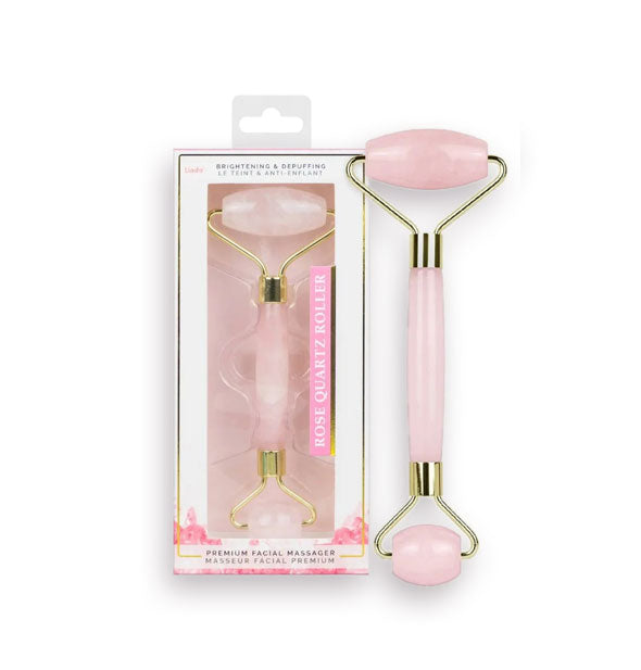Double-ended rose quartz facial roller with gold hardware next to its packaging