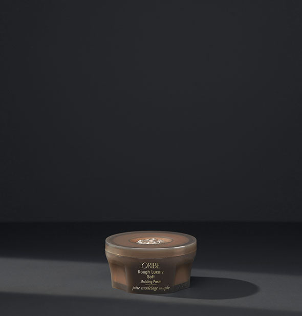 Small brown pot of Oribe Rough Luxury Soft Molding Paste on dark gray background