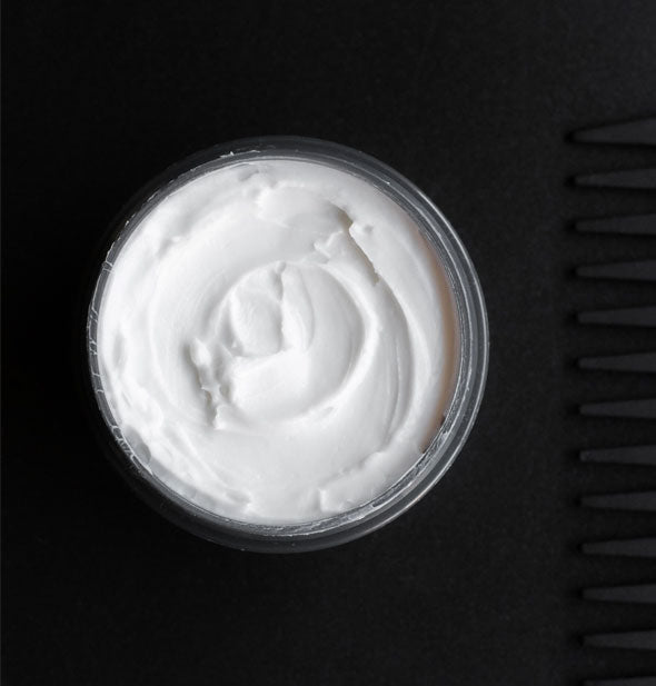 Top view of an opened pot of ColorProof Rule Breaker Defining Wax shows white, creamy product inside and the teeth of a black comb next to it