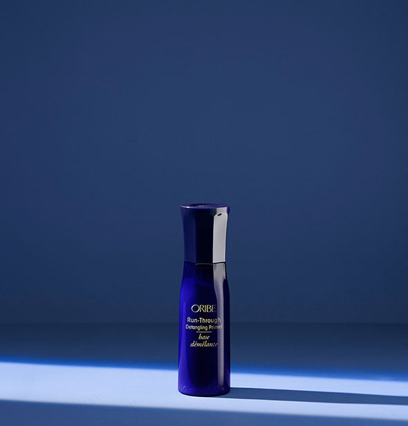 Small royal blue bottle of Oribe Run-Through Detangling Primer on blue background