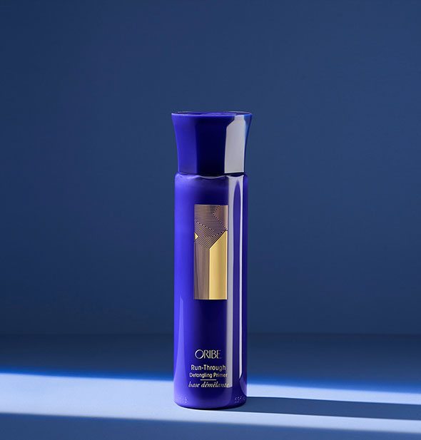 Royal blue bottle of Oribe Run-Through Detangling Primer on blue background