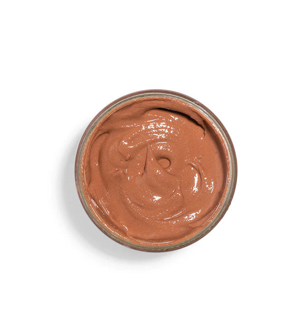 Top view of an opened pot of mud mask shows creamy, reddish-brown product inside