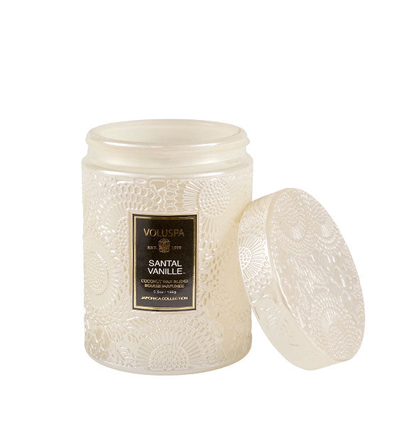 White embossed glass jar Voluspa candle with black label and embossed lid set to the side