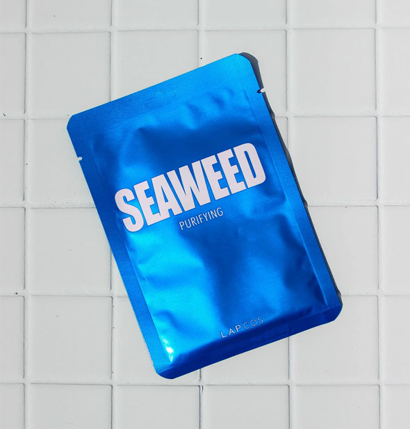 A shiny blue Seaweed Purifying sheet mask pack rests on a white tiled surface
