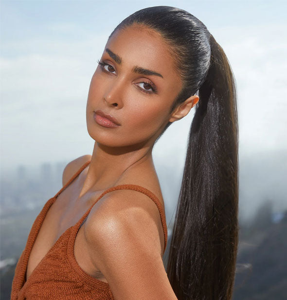 Model with slicked-back high ponytail stands in front of a distant skyline backdrop