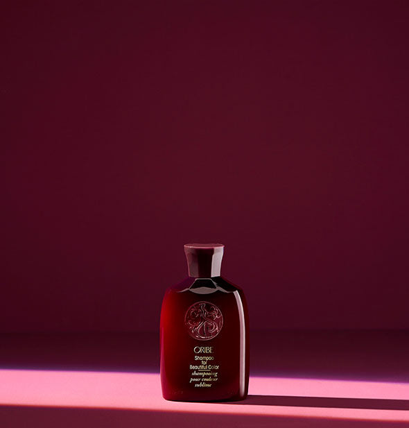 Small dark red bottle of Oribe Shampoo for Beautiful Color on burgundy background