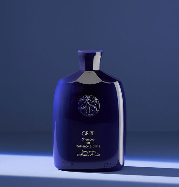 Dark blue bottle of Oribe Shampoo for Brilliance & Shine on blue background