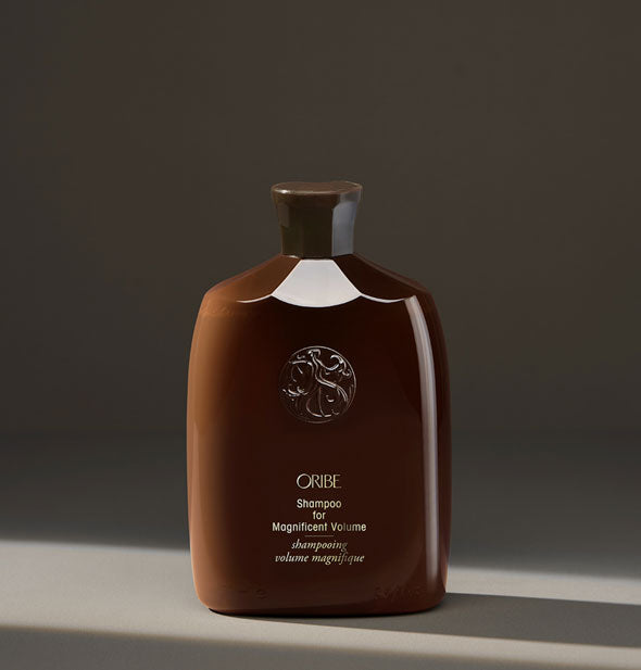 Brown bottle of Oribe Shampoo for Magnificent Volume on dark neutral background