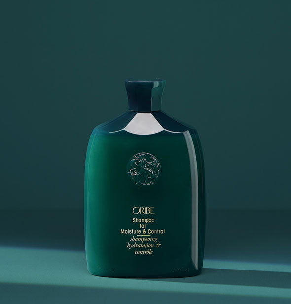 Dark green bottle of Oribe Shampoo for Moisture & Control on teal background