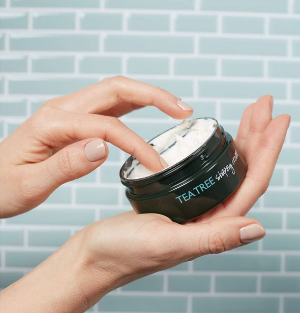 Model dips a finger into a pot of Paul Mitchell Tea Tree Shaping Cream