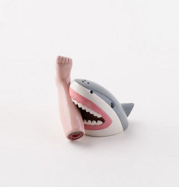 A ceramic salt and pepper shaker set are designed and painted to resemble a shark biting a human leg