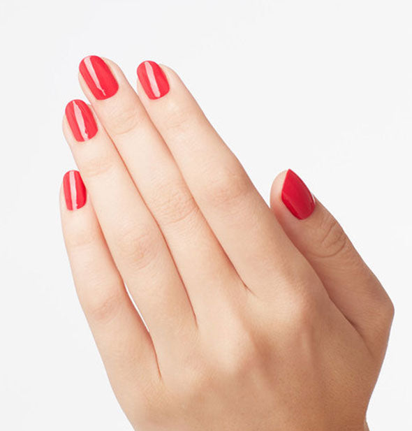 Model's hand wears a coral-magenta shade of nail polish