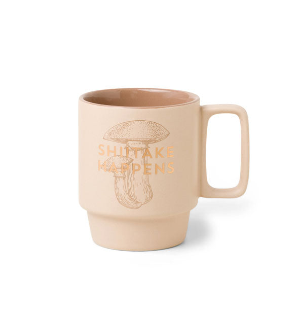 Peach-colored mug with stackable design and square handle says, "Shiitake Happens" in metallic gold foil lettering overtop a light-colored illustration of mushrooms