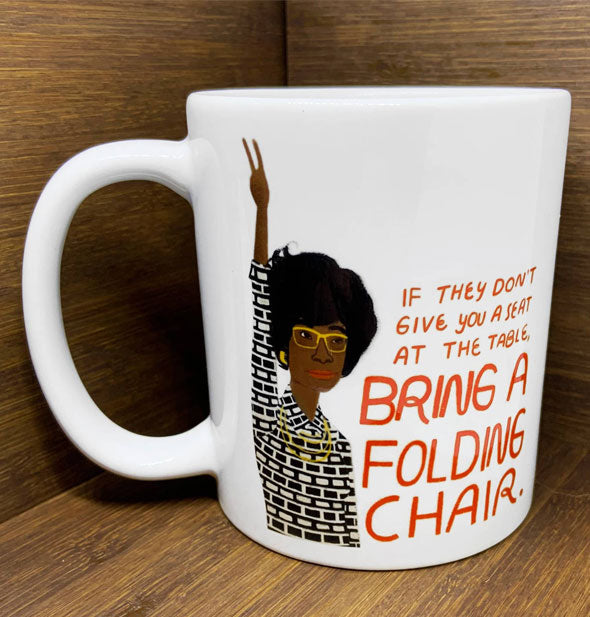 White coffee mug with illustration of Shirley Chisolm says, "If they don't give you a seat at the table, bring a folding chair."