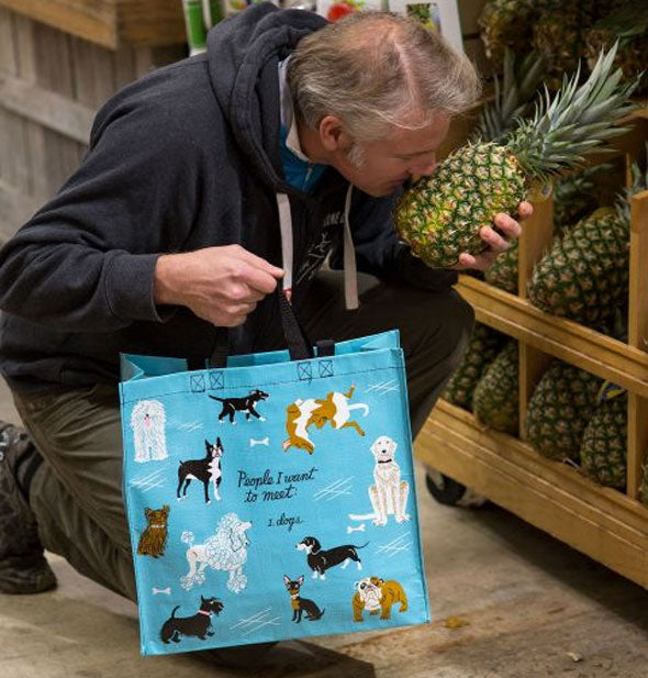 Kneeling man who is smelling a pineapple holds the People I Want to Meet: Dogs Shopper