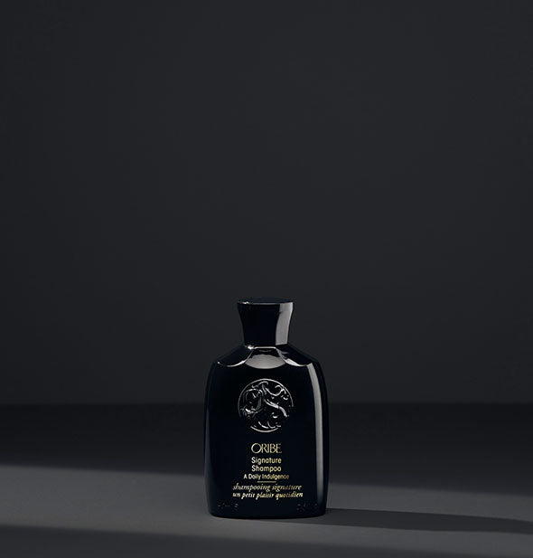 Small black bottle of Oribe Signature Shampoo on dark gray background