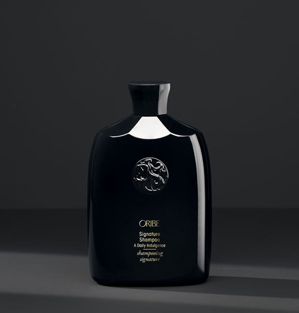 Black bottle of Oribe Signature Shampoo on dark gray background