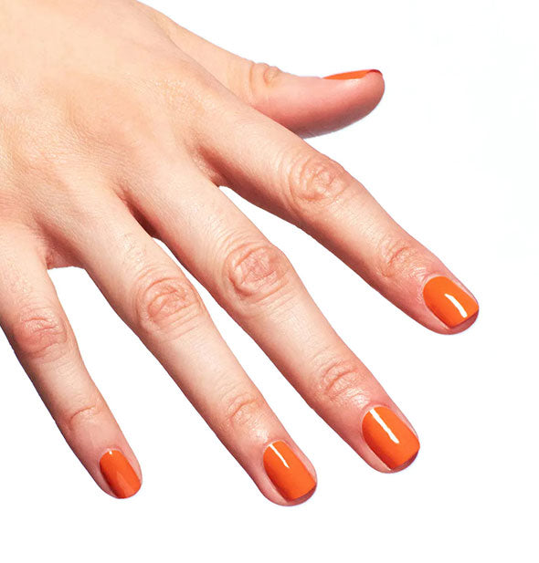 A hand models orange nail polish