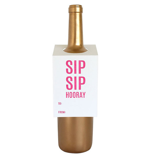 White card that says, "Sip sip hooray" in pink lettering hangs on the shoulder of a gold wine bottle