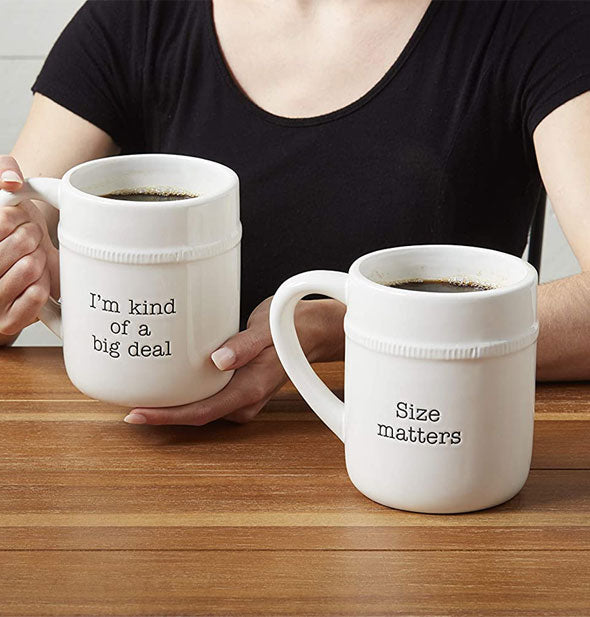 Model poses with two oversized coffee mugs, one of which says, "I'm kind of a big deal," and the other, "Size matters"