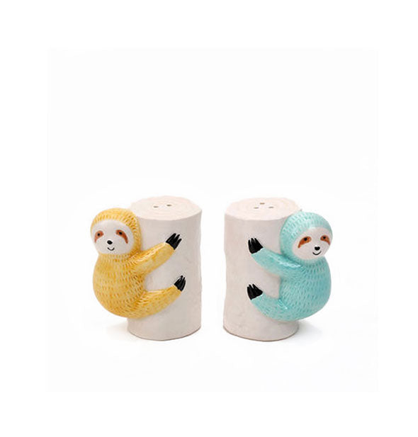 Pair of ceramic salt and pepper shakers resemble two sloths, one yellow and one blue, holding onto tree trunks