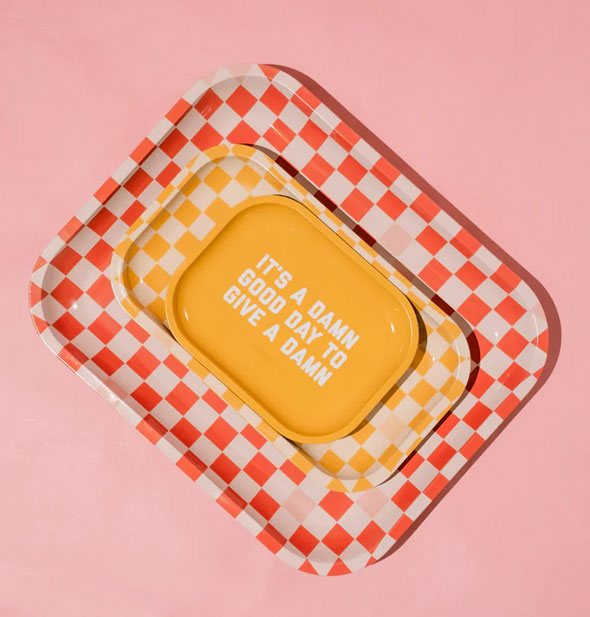 Three rectangular trays with rounded corners are stacked larges to smallest: red checkered on bottom, yellow checkered in the middle, and solid yellow on top with, "It's a damn good day to give a damn" printed in white in its center