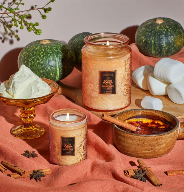 Orange embossed glass jar candles with various spices and botanicals on coral linen