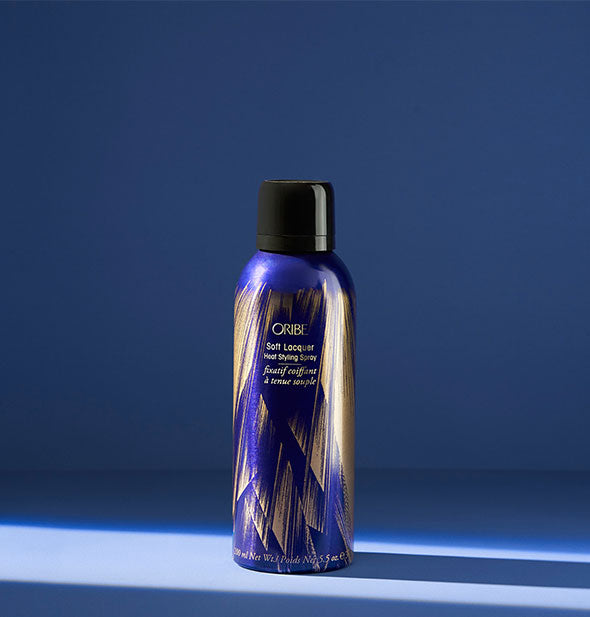 Blue and gold can of Oribe Soft Lacquer Heat Styling Spray on blue background
