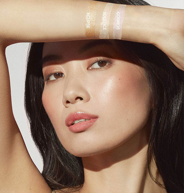 Model with medium-to-light skin tone raises arm painted with three labeled shades of Jane Iredale Glow Time Highlighter Stick