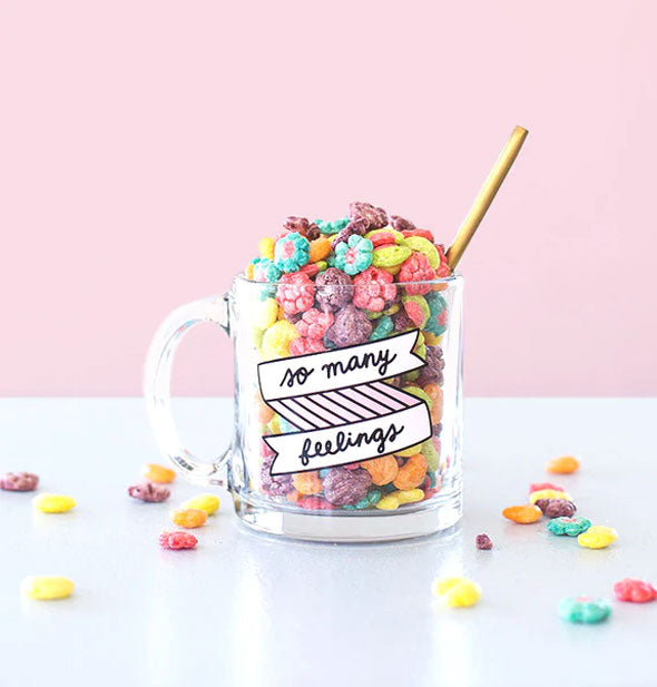 Clear glass So Many Feelings mug is filled with colorful cereal and has a gold spoon handle sticking out of it