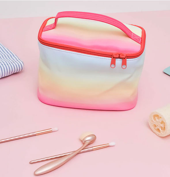 Rainbow bag is staged with skincare items on a pink surface