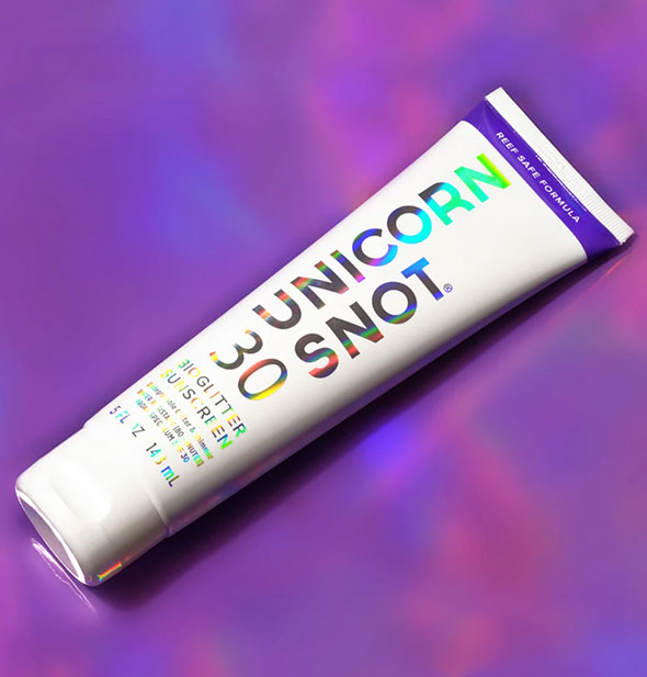 Tube of Unicorn Snot BioGlitter Sunscreen with purple stripe and holographic lettering on a bright purple surface