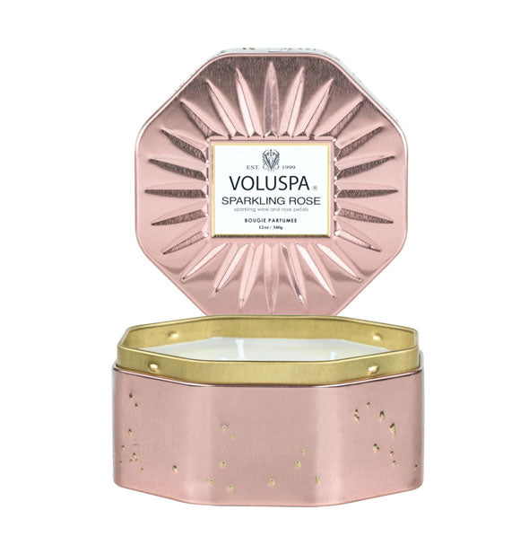 Octagonal pink Voluspa Sparkling Rose tin candle with gold rim and a speckled texture with its embossed lid propped behind