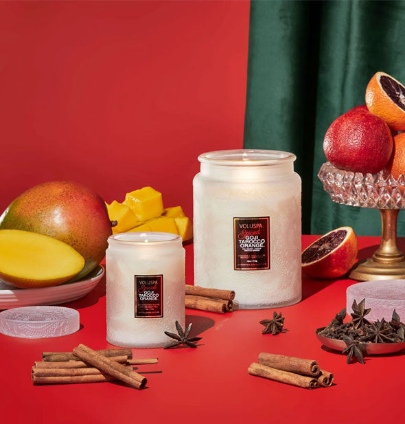 Small and large white embossed glass jar candles are staged with mango, grapefruit, star anise, and cinnamon sticks