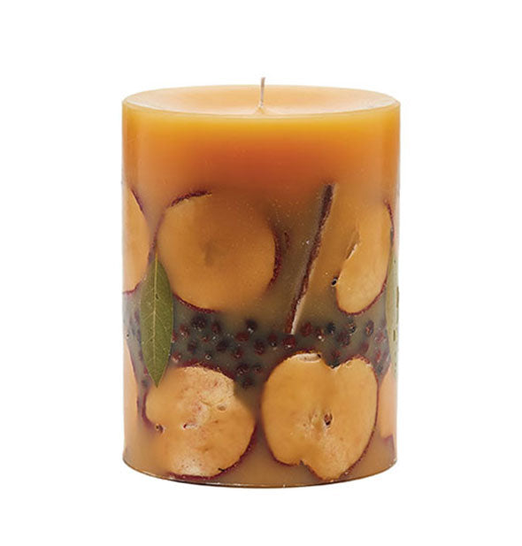 Pillar candle with amber-colored wax and exposed apple slices, cinnamon sticks, bay leaves, and rosehips