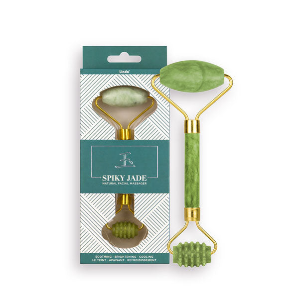 Green jade stone facial roller with one spiky roller end and gold hardware next to its packaging