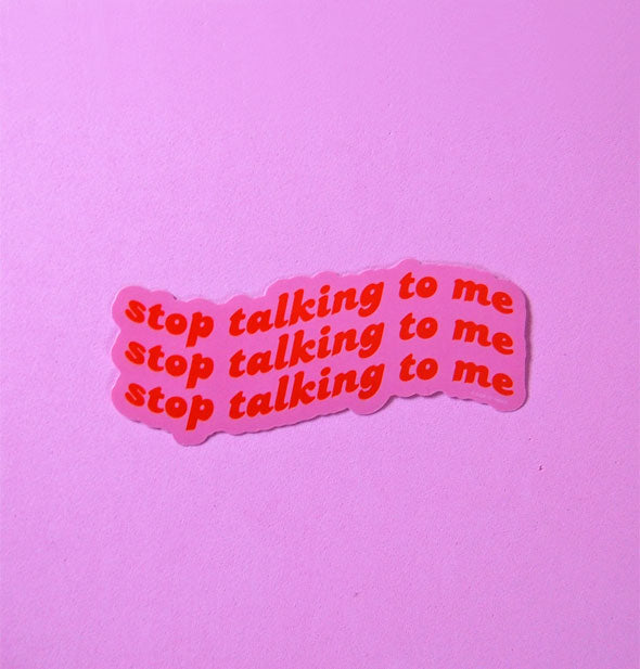 Sticker says, "Stop talking to me" three times in red lettering on a pink background