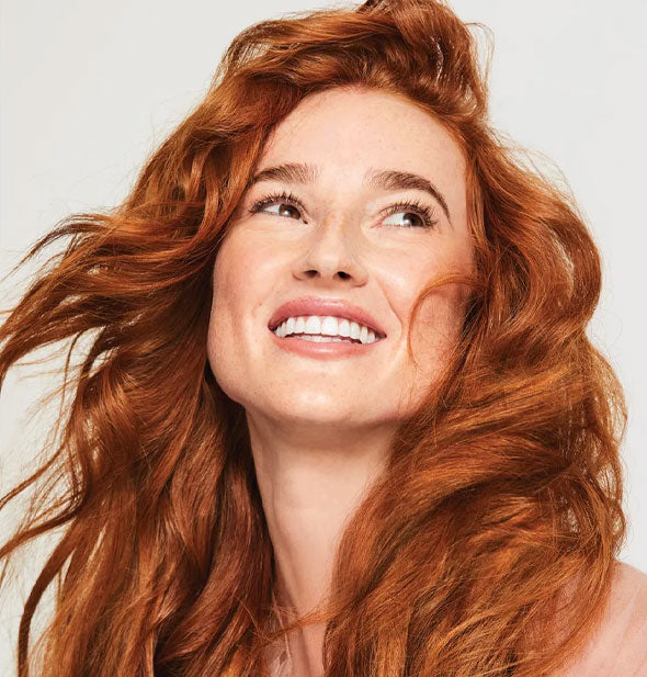 Smiling model with healthy-looking red hair styled in loose, beachy waves