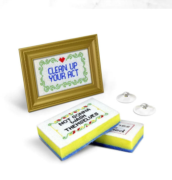 Dish sponges with cross-stitch artwork including the messages, "Clean up your act" and "Not gonna wash themselves" with gold frame and suction cups
