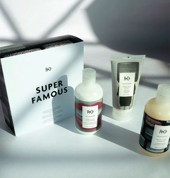 Box and contents of R+Co's Super Famous Kit: Television Perfect Hair Shampoo, Conditioner, and Masque with shadows cast across them