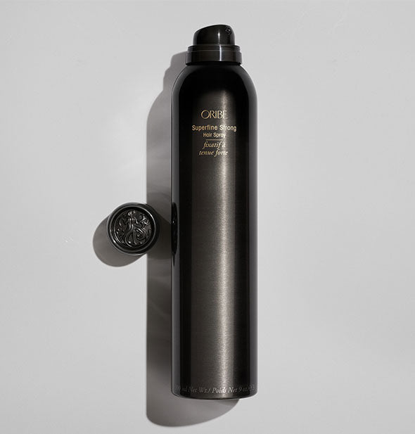 Black can of Oribe Superfine Strong Hairspray with ornate cap to the side