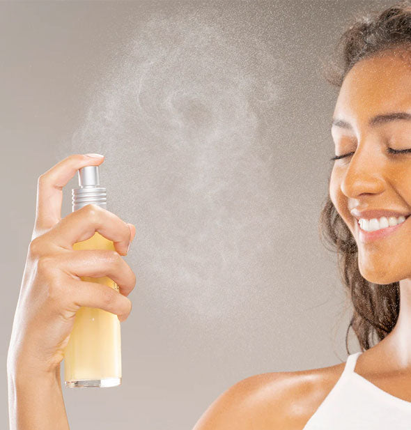 Smiling model mists face with a spritz from a bottle of Super Lettuce Facial Tonic