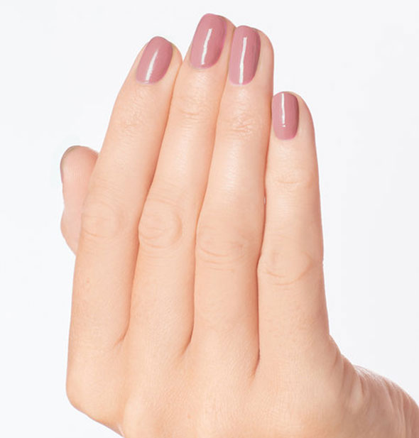 Model's hand wears a muted mauve-pink shade of nail polish