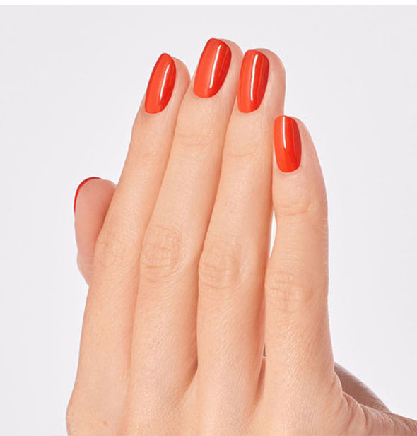 Model's hand wears a shade of red-orange nail polish