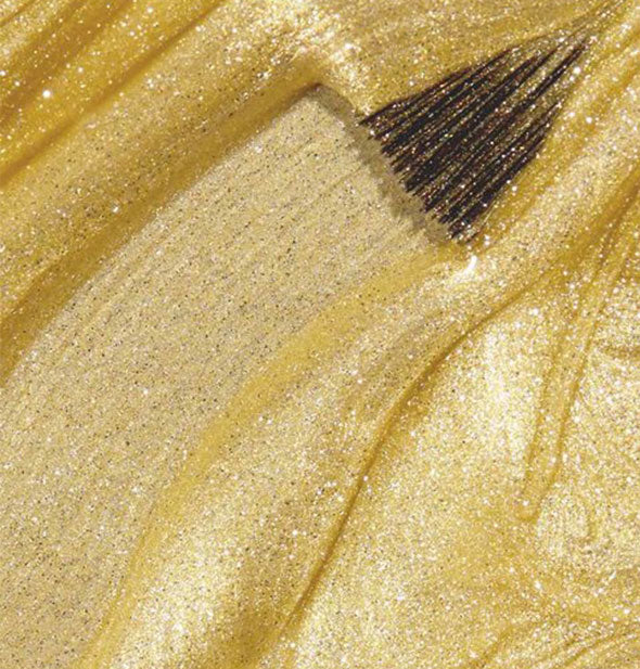 Shimmering yellow-gold nail polish with brush tip drawn through